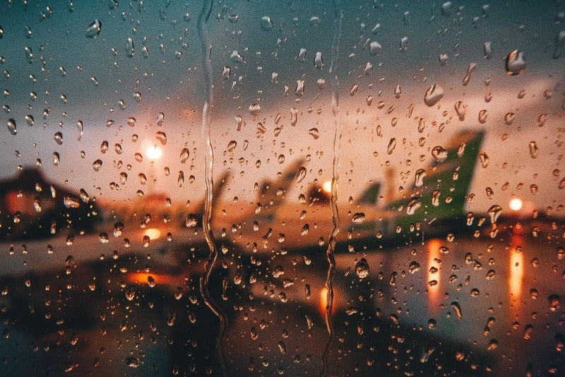 Looking out of a rainy airplane window at wing on runway
