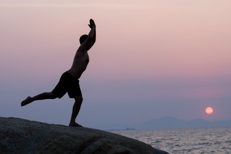 Person doing yoga at sunset by ocean